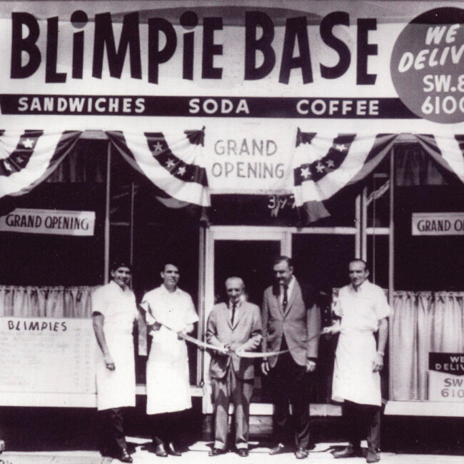 Vintage Blimpie store grand opening with 5 men standing outside the store cutting a ribbon