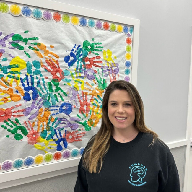 COMPASS founder, Jordanna Spaulding, standing in front of a board with colorful handprints