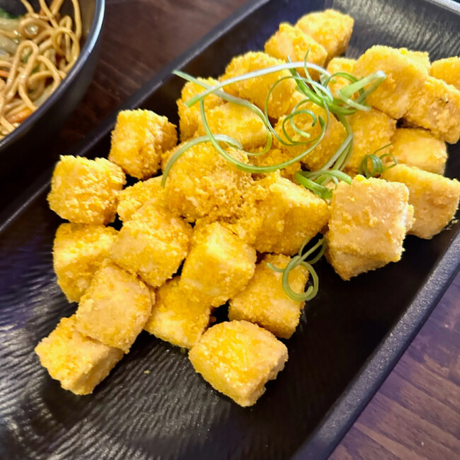 Plate of crispy yellow tofu topped with greens