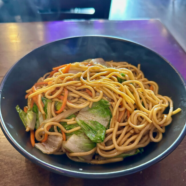 Bowl of steaming noodles with carrots and greens