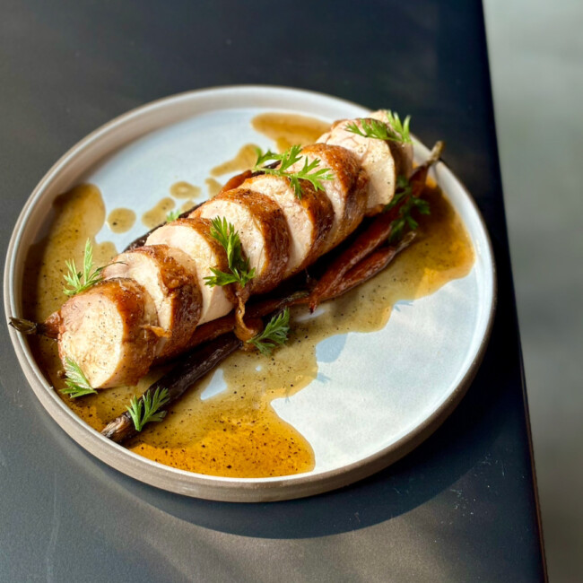 Plate with medallions of meat covered in a brown sauce and garnished with herbs