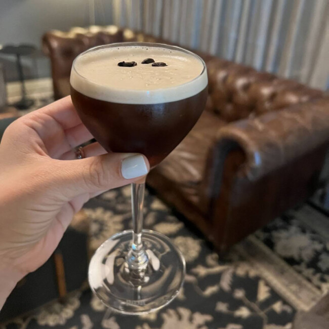Hand holding an espresso martini in front of a couch