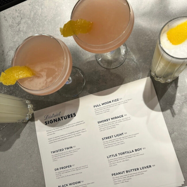 View of two pink cocktails and two yellow cocktails and a cocktail menu