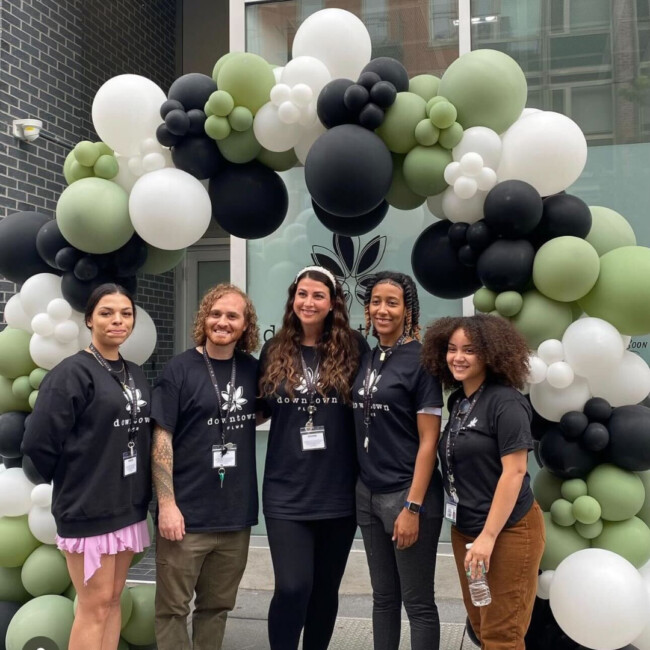 Five people in black downtown FLWR shirts standing in front of a balloon arch with green, white, and black balloons