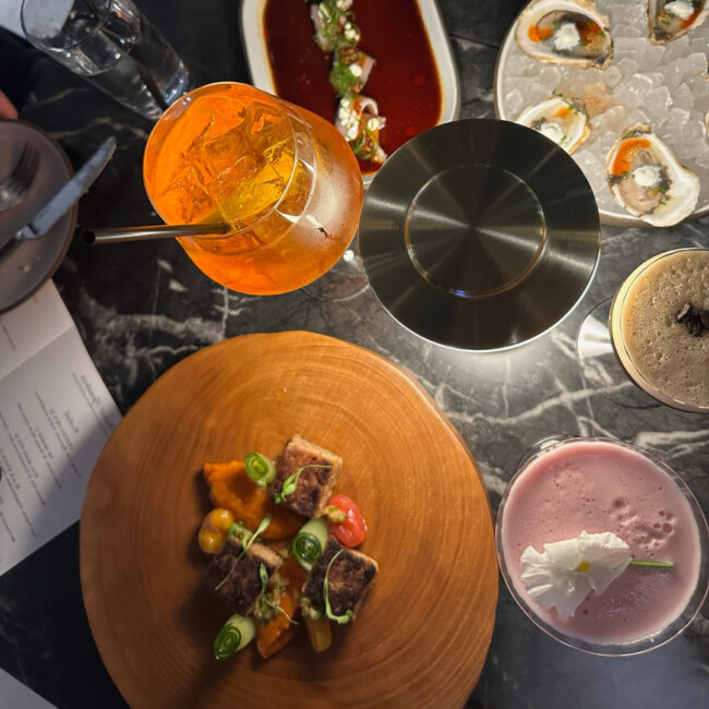 Table with plate of oysters, Aperol spritz, and a few other entrees and drinks